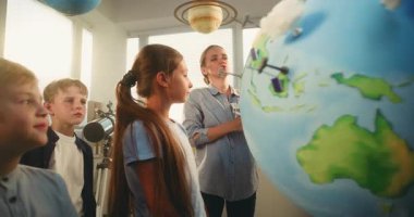 İlköğretim Okulu Öğrencileri Yenilenebilir Enerji Kaynakları Öğreniyor. Dünya Modelini Rüzgâr Türbinleri ve Güneş Panelleri Modelleri ile kullanan Zeki Çocuklar Ekibi 'ne Ekolojiyi Açıklayan Kadın Öğretmen.