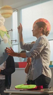 Yenilenebilir Enerji BTMM Sınıfı: İlkokul öğrencileri Dünya 'ya Bulutların Minyatür Modelleri Ekliyor. Akıllı Çeşitli Çocuklara Bilim ve Enerji Kaynaklarını Açıklayan Bayan Öğretmen. Dikey Çekim.