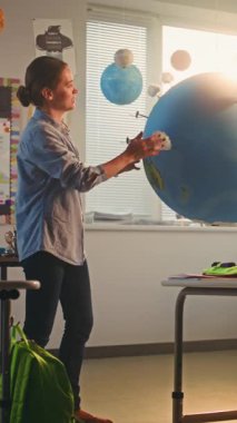 BTMM Yenilenebilir Enerji Sınıfı: Dünya Gezegeni Modelini Kullanan İlkokul Öğrencilerine Enerji Kaynaklarını Açıklayan Kadın Öğretmen. Modern Sınıfta Coğrafya Öğrenen Çeşitli Çocuklar. Dikey Çekim