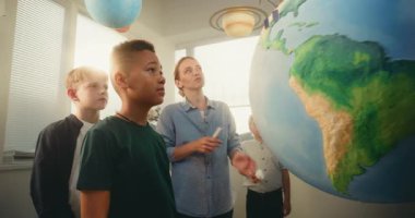 STEM Sınıfı: Yenilenebilir Enerji Kaynaklarını Rüzgar Türbinleri ve Güneş Panelleri ile Dünya Modelleri Kullanan Akıllı Çocuklar Ekibine Açıklayan Kadın Öğretmen. İlkokul Ekoloji Öğrenen Öğrencileri.