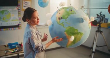 STEM Sınıfı: Modern Sınıfta İlkokul Çocuklarına Çevre Bilimi ve Coğrafya Öğretmenliği Yapan Kadın Öğretmenler. Yenilenebilir enerji kaynaklarını sunan okul çocuğu Dünya Modelini Kullanıyor. Doli Vuruşu.