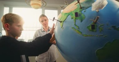 STEM Bilim Dersi: İlkokul çocukları Yenilenebilir Enerji ve Ekoloji okuyor. Dünya 'yı Minyatür Rüzgar Türbinleri ve Güneş Panelleri Modelleri ile Kullanan Akıllı Çeşitli Çocukları Eğiten Kadın Öğretmenler.