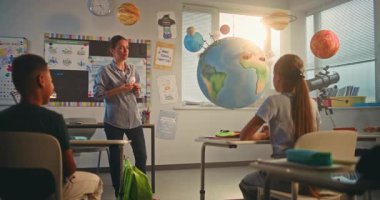 BTMM Yenilenebilir Enerji Sınıfı: Dünya Gezegeni Modelini Kullanan İlkokul Öğrencilerine Enerji Kaynaklarını Açıklayan Kadın Öğretmen. Modern Sınıfta Çeşitli Çocuklar Fen Bilimi Öğreniyor. Yavaş Hareket.