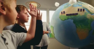 Ekoloji BTMM sınıfı: İlkokul öğrencileri cevap vermek için ellerini kaldırıyor. 3 Boyutlu Rüzgar Türbinleri ve Güneş Panelleri Modelleri ile Dünya 'yı Kullanan Çocuklar Takımına Yenilenebilir Enerji Açıklayan Kadın Öğretmen.