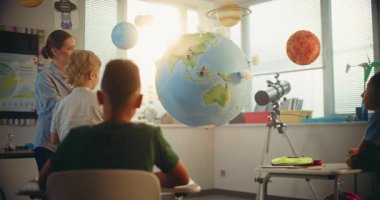 İlkokul çocuğu, Dünya Modelini Kullanarak Sınıfın Önündeki Yeşil Enerji Kaynaklarını Sunar. Sınıfta Fen Sınıfı 'nda Zeki Çeşitli Çocukları Eğiten Kadın Öğretmen. BTMM Eğitim. Yavaş Hareket.