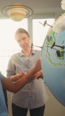 Dünya Modelini Rüzgâr Türbinleri ve Güneş Panelleri 'nin 3 boyutlu Modelleri ile kullanan Yeşil Enerji Kaynaklarını Sunan Kız. İlkokul öğrencileri öğretmenden yenilenebilir enerji öğreniyor. Dikey Çekim.