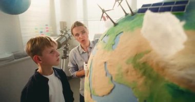 Yenilenebilir Enerji BTMM Sınıfı: İlkokul çocuğu Bulut 'un Dünya' ya Minyatür Modelini Ekliyor. Modern Sınıfta Akıllı Öğrencilere Bilim ve Enerji Kaynaklarını Açıklayan Bayan Öğretmen. Kapat..