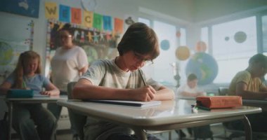 Modern Sınıfta Konsantre İlkokul Çocukları Coğrafya veya Ekoloji Üzerine Okul Sınavı Yazıyor. Masalar Arasında Yürüyen Kadın Öğretmenler Sınav Sürecinde Çeşitli Çocukları Kontrol Ediyor.