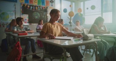 İlkokul çocukları masada oturuyor, öğretmenden ders dinliyor, doğru cevap vermek için ellerini kaldırıyor. Modern Sınıfta Coğrafya veya Bilim Öğrenen Genç Erkekler ve Kızlar Grubu.