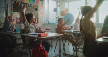 İlkokul çocukları masada oturuyor, öğretmenden ders dinliyor, doğru cevap vermek için ellerini kaldırıyor. Modern Sınıfta Coğrafya veya Bilim Öğrenen Genç Erkekler ve Kızlar Grubu.