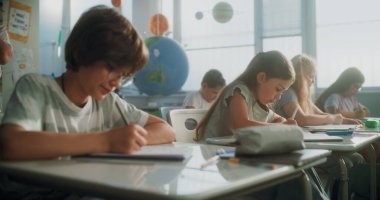 İlkokul öğrencileri Sınav Yazıyor ya da Not Defterlerinde Görev Yapıyor. Modern Sınıfta Sınav Sürecinde Masalar Arasında Yürüyen Bayan Öğretmen, Genç Kızları ve Oğlanları Kontrol Etmek. Sabit Çekim.