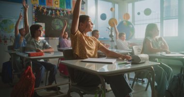 İlkokul çocukları masada oturuyor, öğretmenden ders dinliyor, doğru cevap vermek için ellerini kaldırıyor. Modern Sınıfta Coğrafya veya Bilim Öğrenen Genç Erkekler ve Kızlar Grubu.