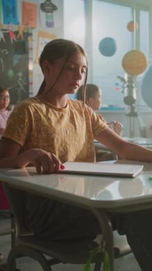 İlkokul çocukları masada oturuyor, öğretmenden ders dinliyor, doğru cevap vermek için ellerini kaldırıyor. Modern Sınıfta Genç Erkekler ve Kızlar Bilim Öğreniyor Grubu. Dikey Çekim.