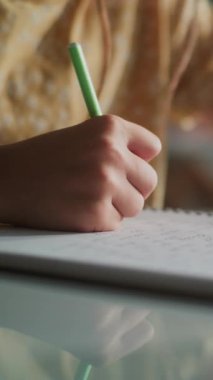 İlköğretim Okulu Kız Yazma Sınavı ya da Not Defterinde Görev Yaparken Yakın Çekim. Arka planda, Modern Sınıfta Okul Sınavı Sırasındaki Odaklanmamış Genç Erkekler ve Kızlar Grubu. Dikey Çekim.