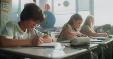 İlkokul öğrencileri Sınav Yazıyor ya da Not Defterlerinde Görev Yapıyor. Modern Sınıfta Sınav Sürecinde Masalar Arasında Yürüyen Bayan Öğretmen, Genç Kızları ve Oğlanları Kontrol Etmek. Sabit Çekim.
