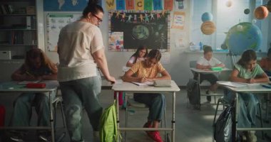 Modern Sınıfta Oturan ve Yenilenebilir Enerji Kaynakları Sınavı Yazan İlkokul Öğrencileri. Masaların Arasında Yürüyen Bayan Öğretmen, Okul Sınavı Sürecinde Genç Erkek ve Kızları Kontrol Etmek