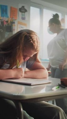 Konsantre İlkokul Çocukları Sınıfta Coğrafya Sınavı Yazıyor. Masalar Arasında Yürüyen Kadın Öğretmenler Sınav Sürecinde Çeşitli Çocukları Kontrol Ediyor. Dikey Çekim.