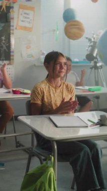 Neşeli çeşitli çocuklar ellerini çırpıyor, dinamik oyun aktiviteleri sırasında öğretmenle etkileşime geçiyor. İlkokul öğrencilerine etkileşimli ders veren bayan öğretmen. Dikey Çekim.