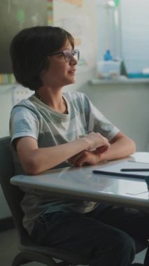 İlkokul çocukları masada oturuyor, konferans dinliyor, doğru cevap vermek için ellerini kaldırıyor. Modern Sınıfta Coğrafya veya Bilim Öğrenen Genç Erkekler ve Kızlar Grubu. Dikey Çekim.