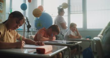 İlkokul öğrencileri Sınav Yazıyor ya da Not Defterlerinde Görev Yapıyor. Modern Sınıfta Sınav Sürecinde Masalar Arasında Yürüyen Bayan Öğretmen, Genç Kızları ve Oğlanları Kontrol Etmek. Doli Vuruşu.