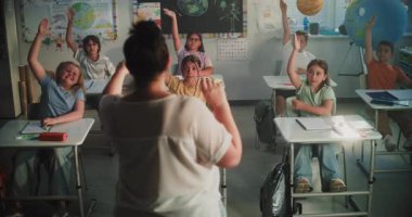 İlkokul öğrencilerine Bayan Öğretmenlik Yönetmenliği Dersi 'ne dönüp, soru soran. Masa başında oturan, cevap vermek için ellerini kaldıran, Modern Sınıfta okuyan zeki çocuklardan oluşan bir takım.