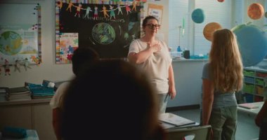 İlkokul çocuklarının ayağa kalkması, ellerini kalbe koymaları, Coğrafya Dersinden Önce Kadın Öğretmenle Ulusal Marşı icra etmeleri. Genç Jenerasyonda Vatanseverliğin Gelişimi