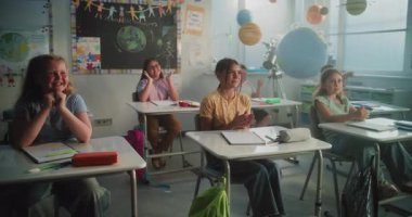 Neşeli Çeşitli Çocuklar Masa başında oturuyor, ellerini çırpıyor, Dinamik Oyunlar sırasında öğretmenle etkileşimde bulunuyor. İlkokul öğrencilerine Etkileşimli Ders Veren Bayan Öğretmen.