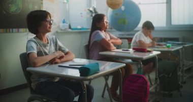 İlkokul çocukları masada oturuyor, öğretmenden ders dinliyor, doğru cevap vermek için ellerini kaldırıyor. Modern Sınıfta Coğrafya veya Bilim Öğrenen Genç Erkekler ve Kızlar Grubu.