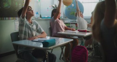 İlkokul öğrencileri masada oturuyor, öğretmenden ders dinliyor, doğru cevabı vermek için ellerini kaldırıyor. Modern Sınıfta Bilim, Coğrafya okuyan Akıllı Çeşitli Çocuklar Takımı.