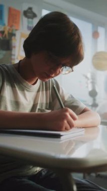 İlkokul öğrencileri Sınıfta Yenilenebilir Enerji Kaynakları Sınavı Yazıyor. Masaların Arasında Yürüyen Bayan Öğretmen, Okul Sınavı Sürecinde Genç Kız ve Oğlanları Kontrol Etmek. Dikey Çekim.