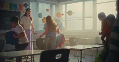 Okul Gününün Başında Genç Kızları ve Oğlanları Selamlayan Bayan Öğretmen. İlkokul öğrencileri Modern Sınıfa giriyor, Masalarda oturuyor ve sırt çantalarını boşaltıyorlar. Yavaş Hareket.