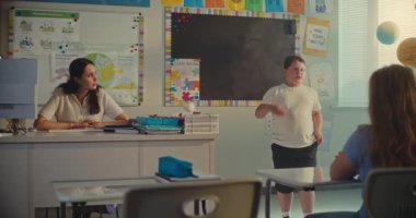 BTMM Yenilenebilir Enerji Sınıfı: İlkokul çocuğu sınıf arkadaşlarının önünde ekoloji ödevini sunuyor ve bayan öğretmen. Sınıfta Bilim Dersinde Masalarda Oturan Genç Erkekler ve Kızlar