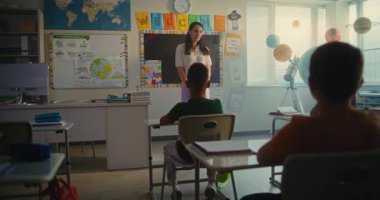 Bayan öğretmen, ilkokul çocuklarıyla dolu sınıfın önünde yeni öğrenciyi tanıtıyor. Masada oturan, el çırpan, dersten önce yeni sınıf arkadaşını selamlayan bir grup farklı çocuk..