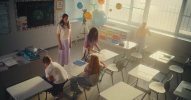 Bayan Öğretmen Dersi Bitiriyordu, Okul Günü 'nde Çeşitli Çocuklar Grubu' na veda ediyordu. Mutlu İlkokul Çocukları sırt çantalarını toplayıp sınıftan ayrılıyorlar. Ağır çekim. Yüksek Açı.