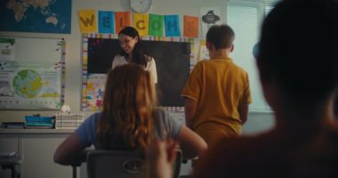 STEM Yenilenebilir Enerji Sınıfı: İlkokul öğrencisini kurula çağıran kadın öğretmen. Yetenekli çocuk, çeşitli çocuklarla dolu sınıfın önünde ekoloji ödevini sunar. Sınıf arkadaşları..