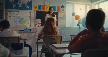 STEM Yenilenebilir Enerji Sınıfı: İlkokul öğrencisini kurula çağıran kadın öğretmen. Yetenekli Kız Çeşitli Çocuklar ve Sınıf Arkadaşlarıyla dolu Sınıfın Önünde Ekoloji Ödevini Sunar.