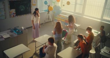 İlkokul çocukları sınıfa giriyor, ders için hazırlanıyor, okul malzemelerini masalara diziyor. Okulun Başında Çeşitli Çocuklar Kadın Öğretmenler Grubu 'nu selamlıyorum. Yüksek Açı.