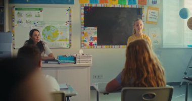 STEM Yenilenebilir Enerji Sınıfı: İlkokul kızı sınıf arkadaşlarının önünde ekoloji ödevini sunuyor ve bayan öğretmen. Sınıfta Fen Dersinde Masalarda Oturan Çeşitli Çocuklar.