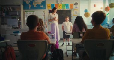 Çevre Bilimi Dersi: Akıllı çocuk sınıfın önündeki yenilenebilir enerji kaynakları ödevini sunuyor. İlkokul öğrencilerine ekoloji eğitimi veren kadın öğretmen. BTMM Eğitim. Yavaş Hareket.