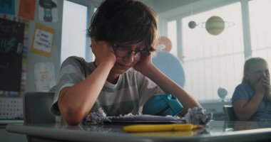 Agresif sınıf arkadaşları onu taciz ederken, kağıtları fırlatırken ve gülerken sınıfın masasında tek başına oturan ilkokul çocuğu. Okul zorbalığı, Akran Tacizi ve Toksik Okul Ortamı.