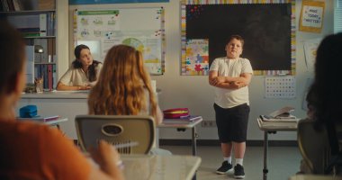 İlkokul çocuğu ekoloji bilgisini sınıfın önünde ve bayan öğretmen olarak gösteriyor. Sınıfta Çevre Bilimleri Dersi sırasında masada oturan zeki çocuklar. BTMM Eğitim. Sabit Çekim.