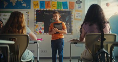 Modern Sınıfta Bilim Dersinde Genç Öğrenciyi Kurula Çağıran Bayan Öğretmen. Dijital tabletli akıllı ilkokul çocuğu sınıfın önünde ekoloji bilgisini gösteriyor. STEM Eğitimi.