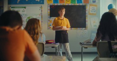 STEM Yenilenebilir Enerji Sınıfı: İlkokul öğrencisini kurula çağıran kadın öğretmen. Yetenekli çocuk, çeşitli çocuklarla dolu sınıfın önünde ekoloji ödevini sunar. Sınıf arkadaşları..