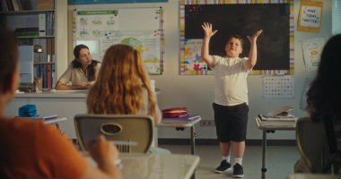 İlkokul çocuğu ekoloji bilgisini sınıfın önünde ve bayan öğretmen olarak gösteriyor. Sınıfta Çevre Bilimleri Dersi sırasında masada oturan zeki çocuklar. BTMM Eğitim. Sabit Çekim.