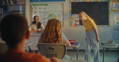 STEM Yenilenebilir Enerji Sınıfı: İlkokul kızı sınıf arkadaşlarının önünde ekoloji ödevini sunuyor ve bayan öğretmen. Sınıfta Fen Dersinde Masalarda Oturan Çeşitli Çocuklar.