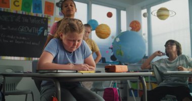 Agresif sınıf arkadaşları onu taciz ederken, Kağıtları fırlatırken ve gülerken, Sınıfta Tek Başına Oturan İlkokul Kızları. Okul zorbalığı, Akran Tacizi ve Toksik Okul Ortamı.