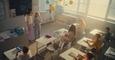 STEM Sınıfı: Ekolojiyi İlkokul Öğrencilerine Eğiten Kadın Öğretmenler Sınıfı. Çeşitli Çocuklar Cevap Vermek İçin Ellerinizi Kaldırın, Akıllı Kız Kurula Gidiyor ve Ödev Sunuyor. Yüksek Açı.