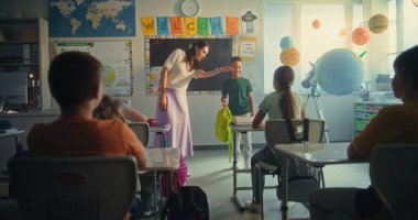 Bayan öğretmen, ilkokul çocuklarıyla dolu sınıfın önünde yeni öğrenciyi tanıtıyor. Masada oturan, el çırpan, dersten önce yeni sınıf arkadaşını selamlayan bir grup farklı çocuk..