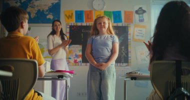 İlkokul öğrencisi utangaç kız sınıf ve öğretmenin önünde ekoloji bilgisi gösteriyor. Modern Sınıfta Çevre Bilimi Dersi sırasında Masalarda oturan Zeki Çocuklar. BTMM Eğitim. Yavaş Hareket.