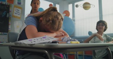 İlkokul öğrencisinin yalnız başına masasında oturması ve sınıf arkadaşları ona zorbalık yaparken ağlaması, gülmesi ve kağıtları fırlatması. Okul zorbalığından, arkadaş tacizinden ve duygusal tacizden muzdarip kız.